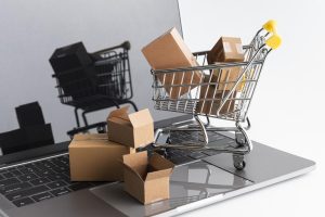 Miniatura de carrinho de compras e caixas de papel em cima de um teclado de notebook.